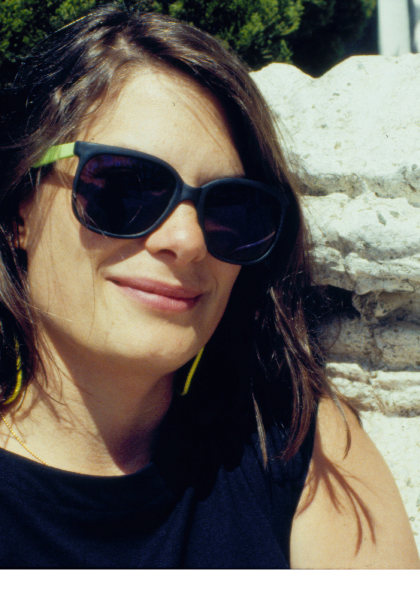 Close-up photo of a brown-haired woman next to a gargoyle-like creature made of stone; she is wearing sunglasses.